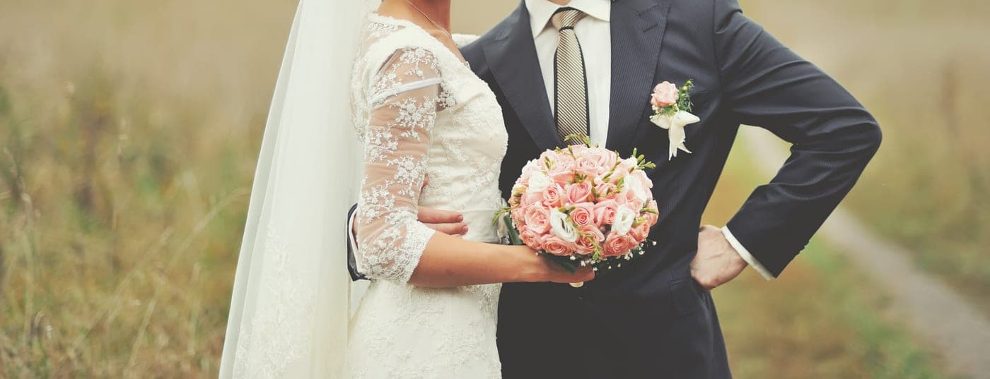 Brautpaar im Feld, die Braut mit Brautstrauß, steht für den Hochzeitsplanungs-Service aijo.hochzeit