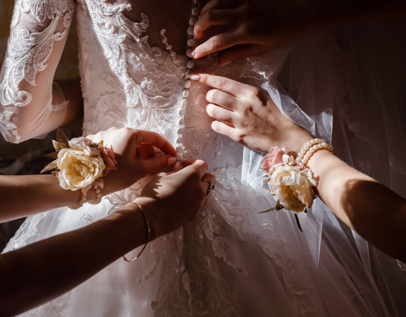 Bridesmaid helping bride fasten corset and getting her dress, preparing bride in morning for the wedding day. Bridesmaid helping bride fasten corset and getting her dress, preparing bride in morning for the wedding day.